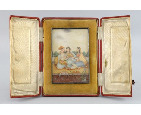 19th century Indian miniature painting on ivory depicting a man and two women seated on a golden carpet, the man smoking a ho