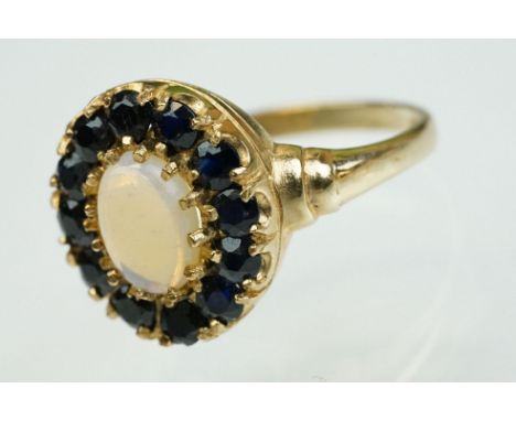 Opal and sapphire 9ct yellow gold oval cluster ring, the cabochon cut milky precious white opal (possibly a moonstone) measur