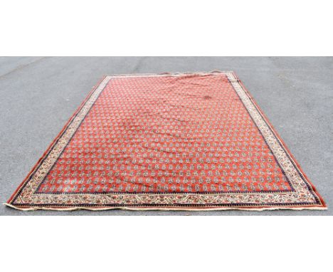 A Persian machine woven wool carpet, decorated with an all over Paisley design against a red ground, 336 x 238cm.