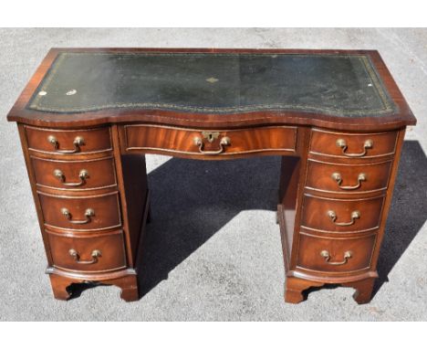 A reproduction mahogany veneered serpentine fronted kneehole desk, with green leather inset top above an arrangement of thirt