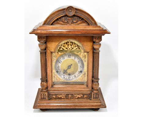 A late 19th century carved walnut mantel clock, the arched top with moulded detail above the brass face and silvered chapter 