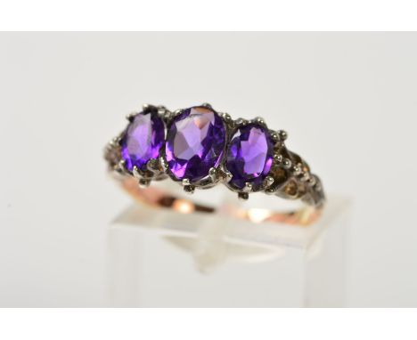 AN AMETHYST RING, designed as three graduated oval amethysts within claw settings, to the shaped and beaded shoulders, stampe
