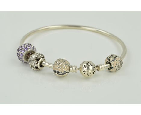 A PANDORA CHARM BANGLE, the circular bangle with Pandora clasp, one non Pandora purple paste charm, two white enamel flower c