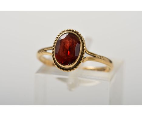 A 9CT GOLD GARNET RING, designed as an oval garnet within a collet setting to the rope twist surround to the bifurcated shoul