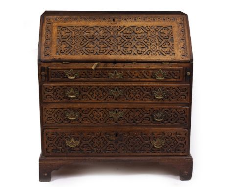 A GEORGIAN OAK  BUREAU having extensive carved geometric decoration, fall front opening to reveal pigeon holes and drawers ab