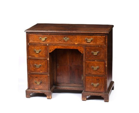 A QUEEN ANNE STYLE FIGURED WALNUT AND MAHOGANY VENEERED KNEEHOLE DESK with an arrangement of seven feather banded drawers aro