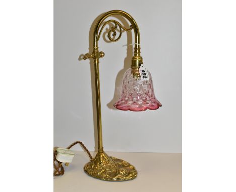 A BRASS TABLE/DESK LAMP, in art nouveau style, with foliate scroll under arched neck, cast floral decoration to the base and 