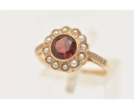 A YELLOW METAL GEM SET CLUSTER RING, centring on a circular cut garnet, milgrain collet set within a surround of split pearls