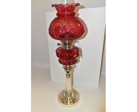 A VICTORIAN STYLE CRANBERRY COLOURED GLASS OIL LAMP, with circular silver coloured Corinthian column pedestal base and Hinks 