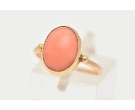 A YELLOW METAL CORAL RING, designed with an oval coral cabochon, in a collet setting, measuring approximately length 12.4mm x