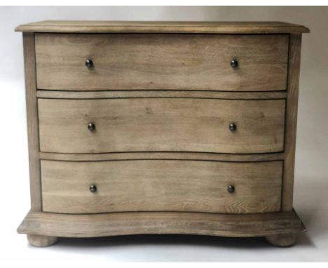 COMMODE, Continental style limed oak of serpentine outline with three long drawers and bun supports, 100cm x 48cm x 81cm H.