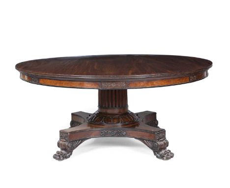 A William IV circular mahogany table with a heavy reeded column stem, platform base with four lion's paw feet and inset brass