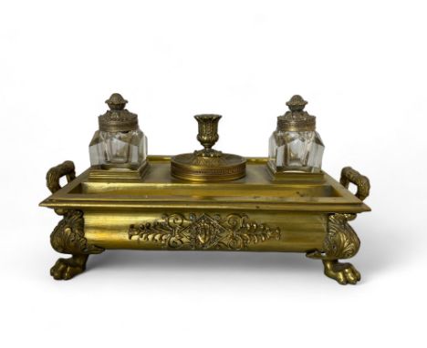 A Regency gilt brass ink stand Of rectangular ogee form, with two cut glass ink pots and a central removable candlestick; wit