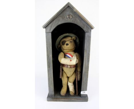 An early 20th Century hump back teddy bear in a WW1 uniform with button eyes, in a wooden sentry box , H. 52cm.