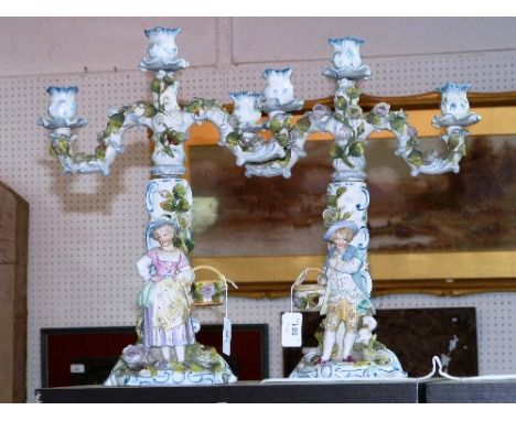 A pair of continental porcelain three-light figural Candelabra, decorated in colours and applied with flowers on scroll bases