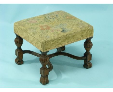 An overstuffed wool-work tapestry Footstool, on a carved walnut base, 18in (46cm) wide.