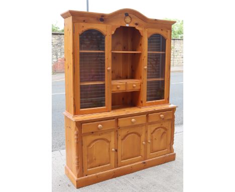 A pine dresser, the upper part fitted with an arrangement of shelves &amp; two small drawers enclosed by a glazed door to eit