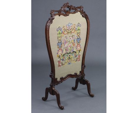 A Victorian carved mahogany firescreen, the pierced foliate scroll frame inset gros-point needlework panel, &amp; on four ree