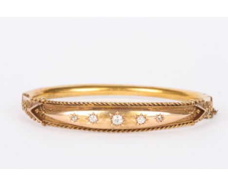 An Edwardian gold coloured metal stiff bangle
set with five graduated diamonds in gypsy setting with rope twist design to bor