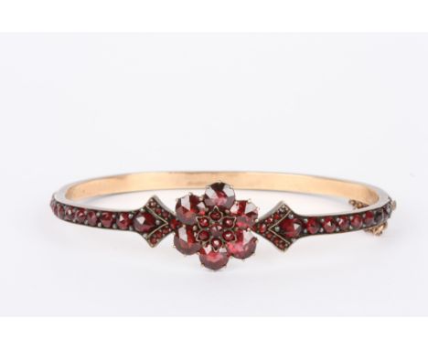 A Bohemian garnet stiff bangle 
the entire band set with garnets in claw setting on gold coloured metal base, with floral sha