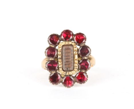 A gold and garnet mourning ring
set with a central panel of woven hair surrounded by ten faceted garnets, set on a later 9ct 