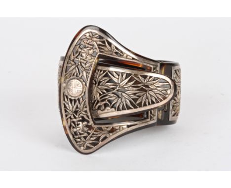 An early 20th century Oriental tortoiseshell and white metal bangle
with hinged clasp of buckle form, the white metal mounts 