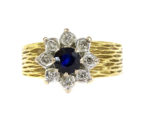 A gold sapphire and diamond flower cluster ring, c.1980, a circular mixed cut sapphire, claw set to surround of eight cut dia