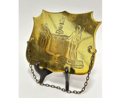 A Georgian brass shield shaped plaque with two male bearded native figures holding clubs and shield with three covered cups a