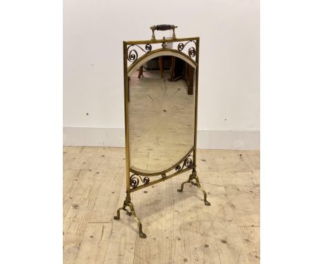 An Edwardian brass mirrored fire screen, with turned handle over scrolling decoration to frame enclosing a bevelled mirror pl