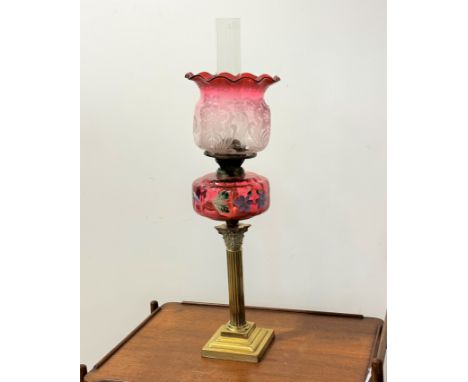 A Victorian corinthian brass cast fluted column oil lamp with cranberry glass overpainted and enamelled floral reservoir and 