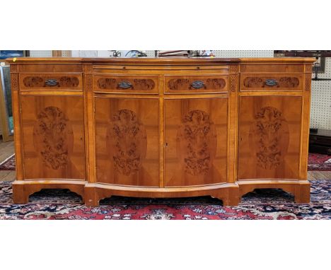 A modern veneered burred yew sideboard, the shaped frontage with four drawers and four cupboard doors, supported on bracket f