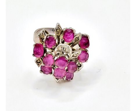 A ruby cluster ring, set with mixed cut rubies, with leaf motif detail inset with small white stones, white metal shank marke