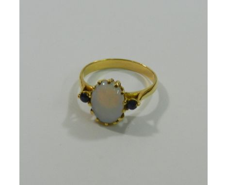 A yellow metal opal and sapphire three stone ring, the oval opal cabochon in claw setting flanked by two small round mixed cu