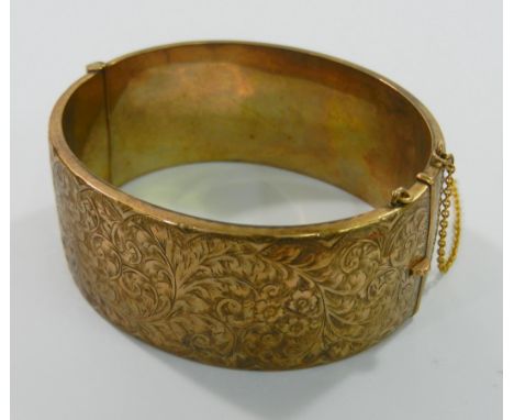 A 9 carat gold hinged bangle with chased scrolling floral and foliate design, 26mm wide, Chester 1959, 33g gross CONDITION RE