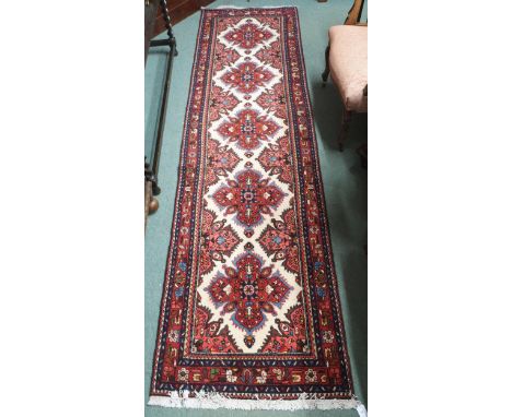 A cream ground Hamadan runner with five red flower head medallions, pink spandrels and multicoloured border, 288cm long x 78c
