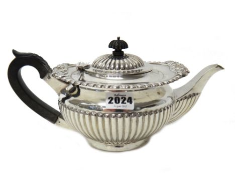 A silver teapot, of compressed circular form, with partly fluted decoration, a boldly gadrooned rim and with ebonised fitting