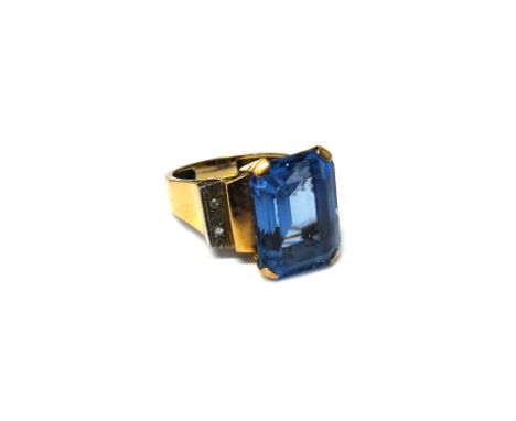 A gold ring, claw set with a cut cornered rectangular step cut synthetic blue spinel at the centre, between diamond two stone