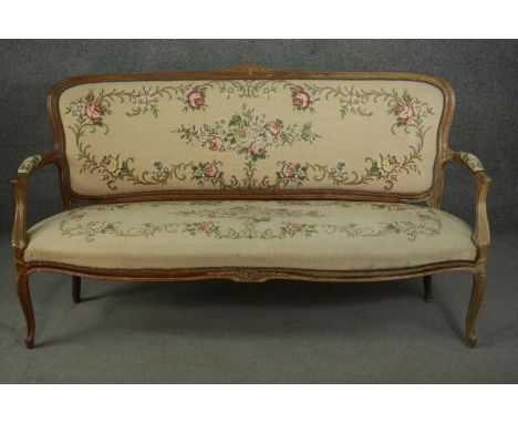 A Louis XV style French walnut canape sofa, the needlepoint upholstery with foliate designs on an ivory ground, with open arm