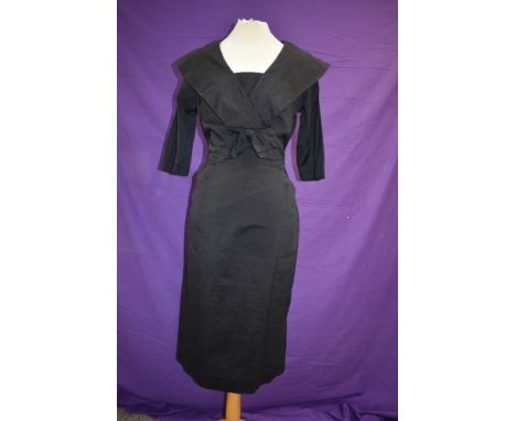 A 1950s black dress having fitted skirt and large portrait collar with bow to front.