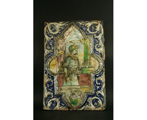 A PERSIAN POTTERY TILE painted with a three quarter length figure of a nobleman, on a moulded cartouche, set on a blue ground