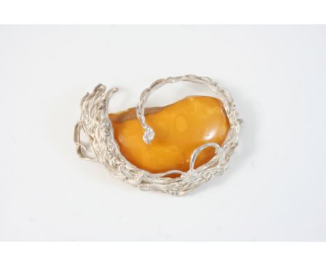 AN AMBER AND SILVER BROOCH set with a section of amber in silver openwork mount, 9cm. wide.