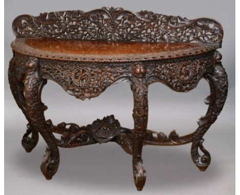 A BOMBAY BLACKWOOD CONSOLE TABLE the semi circular top on bold cabriole legs with animal mask heads, all typically carved and