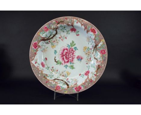 A FAMILLE ROSE SHALLOW BASIN boldly painted with a central peony and flowering shrubs issuing from the cods row border, Qianl