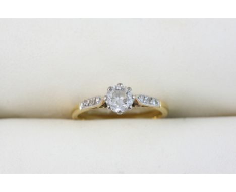 A DIAMOND SOLITAIRE RING set with a circular-cut diamond with three small diamonds set to each shoulder, in gold. Size K.