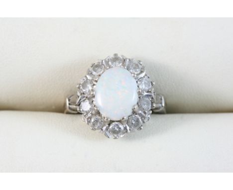 AN OPAL AND DIAMOND CLUSTER RING the oval-shaped cabochon white opal is set within a surround of circular-cut diamonds, in 18