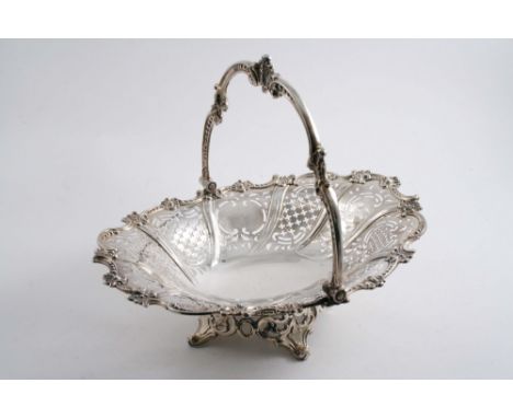 A VICTORIAN SWING-HANDLED CAKE BASKET of shaped oval outline with an ornate border & feet, the sides pierced with crosslets &