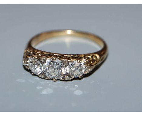 A diamond three-stone ring, claw-set in yellow metal with scrolled mount, size M.
