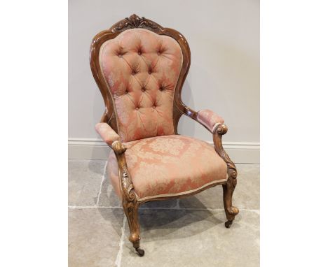 A late Victorian carved walnut button back salon chair, the waisted button back with a foliate carved crest, extending to out