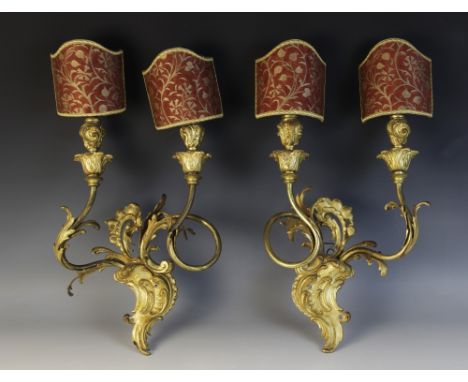 A pair of Rococo style gilt brass twin branch wall sconces, the foliate 'C' scroll back plates supporting twisted arms with a