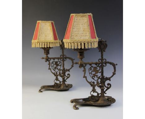 A pair of wrought iron desk lamps in the Medieval manner, each with pierced supports and raised on a cast lyre shaped base, w